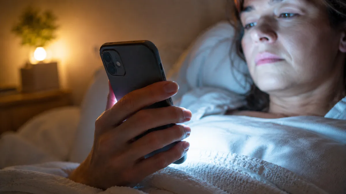 Mano agarrando un celular de noche, luz de pantalla en la cara